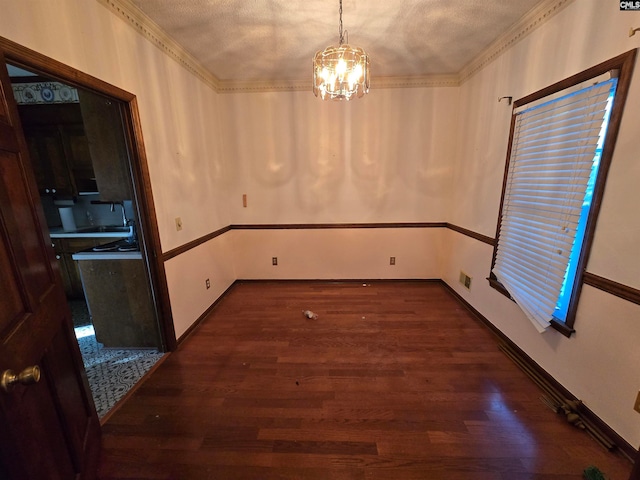 unfurnished dining area with a textured ceiling, crown molding, dark wood-type flooring, sink, and an inviting chandelier