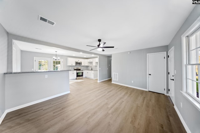 unfurnished living room with ceiling fan with notable chandelier, light wood-type flooring, and sink