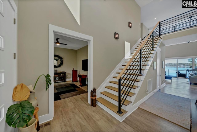 stairs with hardwood / wood-style floors, a towering ceiling, and ceiling fan