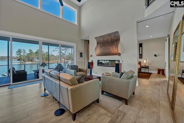 living room with a water view, light hardwood / wood-style floors, and a high ceiling