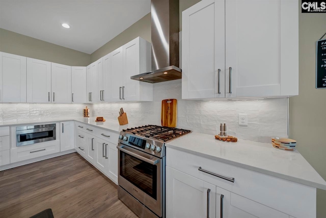 kitchen with white cabinets, light hardwood / wood-style flooring, wall chimney exhaust hood, decorative backsplash, and stainless steel appliances