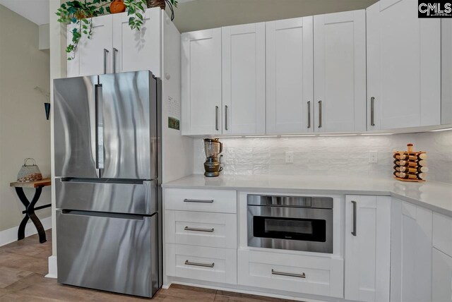 kitchen with backsplash, white cabinets, light hardwood / wood-style floors, and appliances with stainless steel finishes