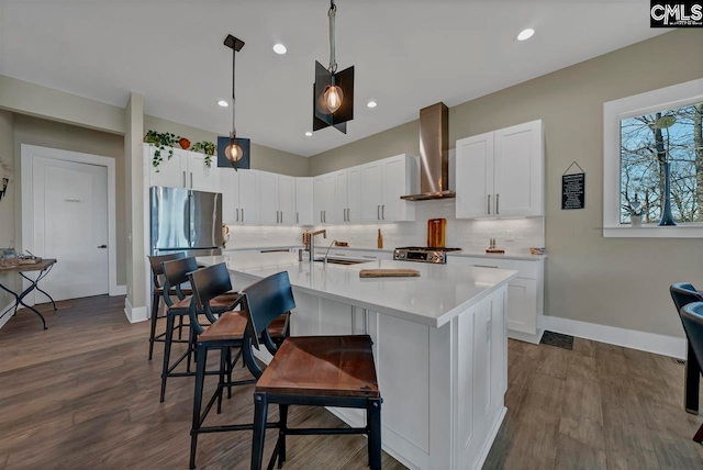 kitchen with a breakfast bar, wall chimney range hood, a center island with sink, dark hardwood / wood-style floors, and white cabinetry