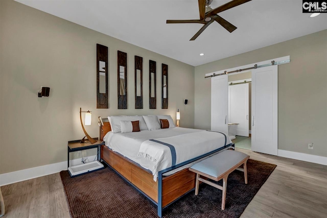 bedroom with hardwood / wood-style flooring, ceiling fan, and a barn door