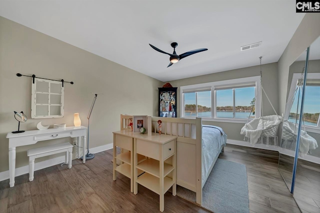 bedroom with ceiling fan, a barn door, a water view, and light hardwood / wood-style flooring