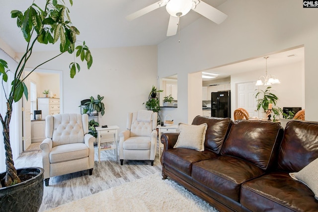 living room featuring high vaulted ceiling, light hardwood / wood-style floors, and ceiling fan with notable chandelier