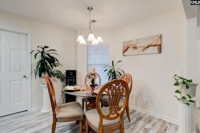 dining space featuring light hardwood / wood-style flooring, a textured ceiling, and an inviting chandelier