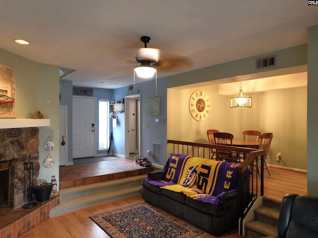 living room featuring hardwood / wood-style floors, ceiling fan, and a stone fireplace