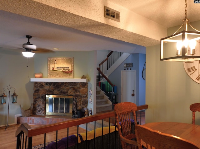 dining room with wood-type flooring, ceiling fan with notable chandelier, a textured ceiling, and a stone fireplace