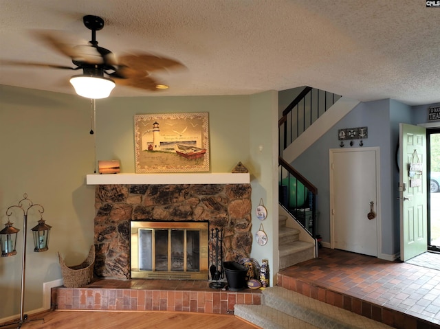 unfurnished living room featuring a stone fireplace, ceiling fan, a textured ceiling, and hardwood / wood-style flooring