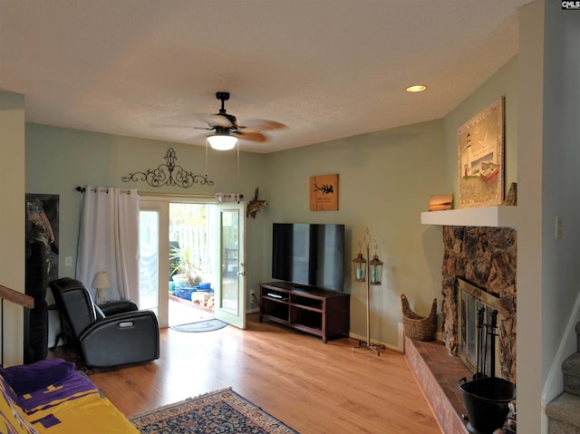 living room featuring ceiling fan, a stone fireplace, and light hardwood / wood-style flooring