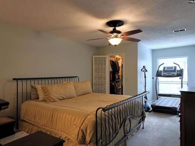 carpeted bedroom featuring a walk in closet, ceiling fan, a closet, and a textured ceiling