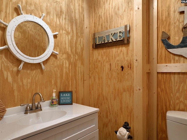 bathroom with vanity, toilet, and wooden walls