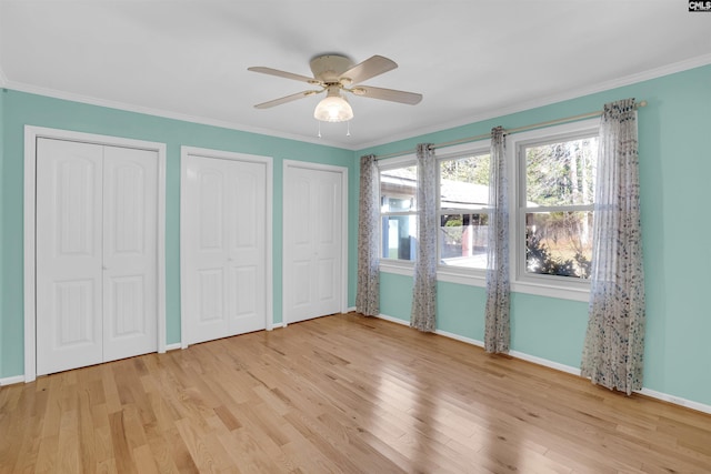 unfurnished bedroom featuring ceiling fan, light wood-type flooring, crown molding, and two closets