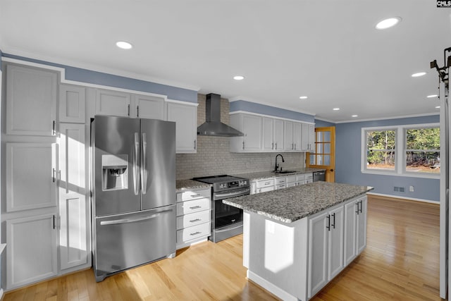 kitchen featuring light stone counters, wall chimney exhaust hood, stainless steel appliances, and light wood-type flooring