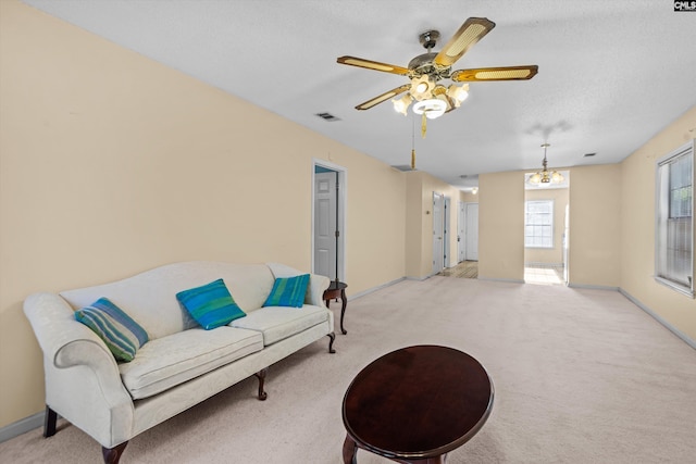 sitting room featuring a textured ceiling, light colored carpet, and ceiling fan with notable chandelier