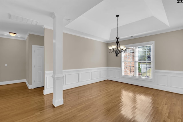 unfurnished room with ornate columns, ornamental molding, a raised ceiling, an inviting chandelier, and hardwood / wood-style floors