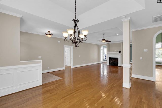 unfurnished living room with decorative columns, crown molding, ceiling fan with notable chandelier, and hardwood / wood-style flooring