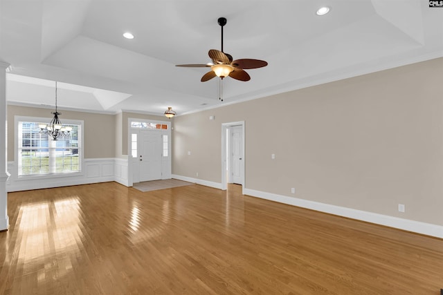 unfurnished living room with a raised ceiling, ornamental molding, ceiling fan with notable chandelier, and hardwood / wood-style flooring