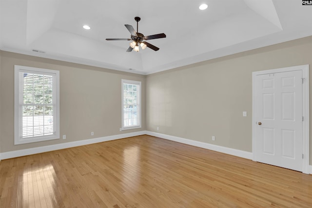 empty room with plenty of natural light, ceiling fan, a raised ceiling, and light hardwood / wood-style flooring