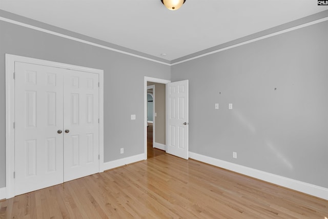 unfurnished bedroom featuring a closet, crown molding, and light hardwood / wood-style flooring