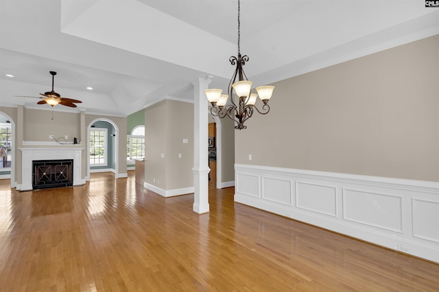 unfurnished living room featuring decorative columns, ornamental molding, ceiling fan with notable chandelier, a raised ceiling, and light hardwood / wood-style flooring