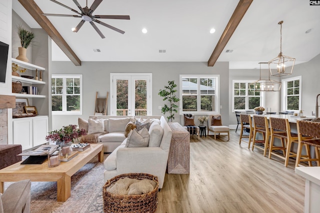 living room with beamed ceiling, ceiling fan with notable chandelier, and light wood-type flooring