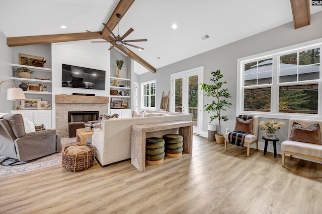 living room with french doors, ceiling fan, lofted ceiling with beams, light hardwood / wood-style floors, and a stone fireplace