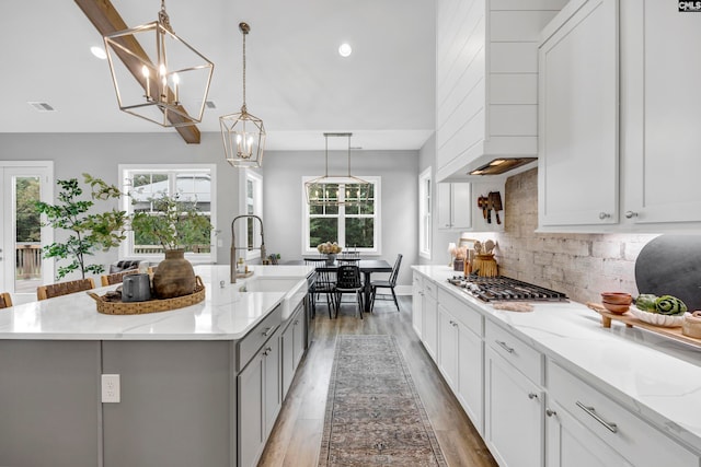 kitchen with stainless steel gas stovetop, a center island with sink, sink, hanging light fixtures, and light stone countertops