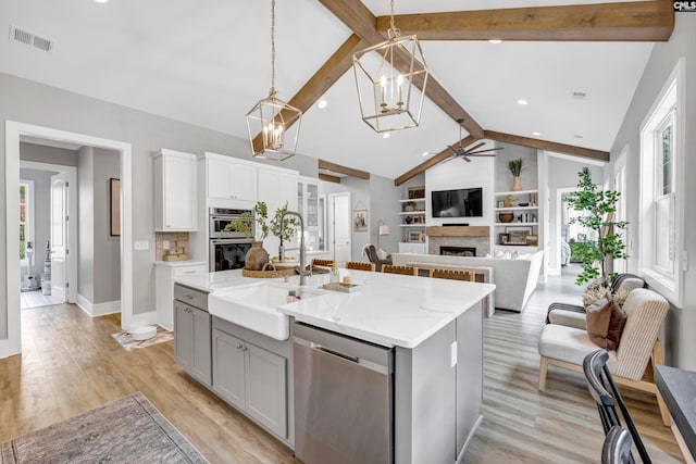 kitchen featuring light stone countertops, appliances with stainless steel finishes, decorative light fixtures, light hardwood / wood-style flooring, and an island with sink