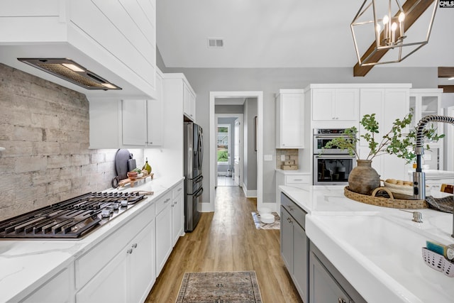 kitchen with sink, light hardwood / wood-style flooring, decorative light fixtures, white cabinets, and appliances with stainless steel finishes