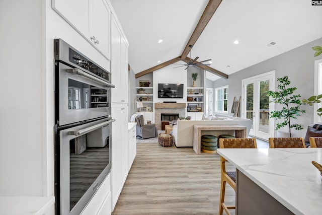 kitchen with light stone countertops, double oven, lofted ceiling with beams, light hardwood / wood-style flooring, and white cabinets