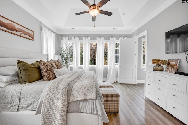 bedroom with ceiling fan, light hardwood / wood-style floors, and a tray ceiling