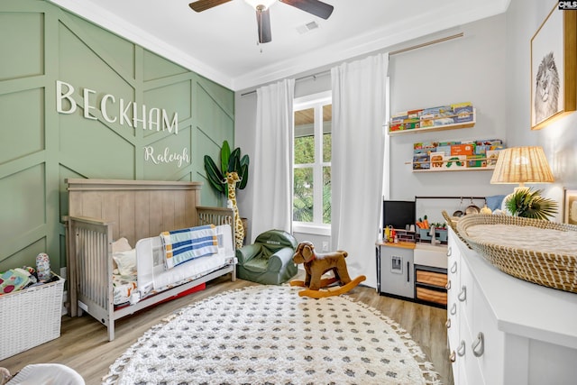 interior space with light wood-type flooring, a nursery area, ceiling fan, and crown molding