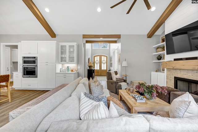 living room featuring ceiling fan, beam ceiling, light hardwood / wood-style floors, and a fireplace