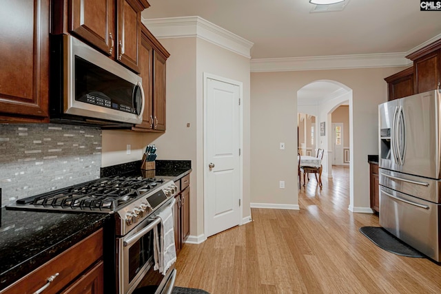 kitchen featuring decorative backsplash, dark stone countertops, ornamental molding, appliances with stainless steel finishes, and light hardwood / wood-style floors