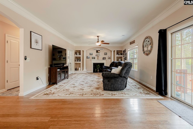 unfurnished living room featuring built in shelves, light hardwood / wood-style flooring, ceiling fan, and ornamental molding