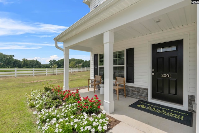 view of exterior entry featuring a lawn, a rural view, and covered porch