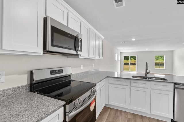 kitchen with sink, light wood-type flooring, appliances with stainless steel finishes, light stone counters, and white cabinetry