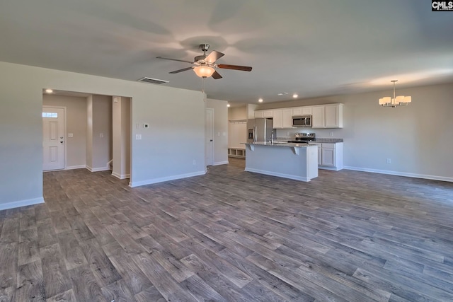 kitchen with appliances with stainless steel finishes, ceiling fan with notable chandelier, a kitchen island with sink, wood-type flooring, and white cabinetry