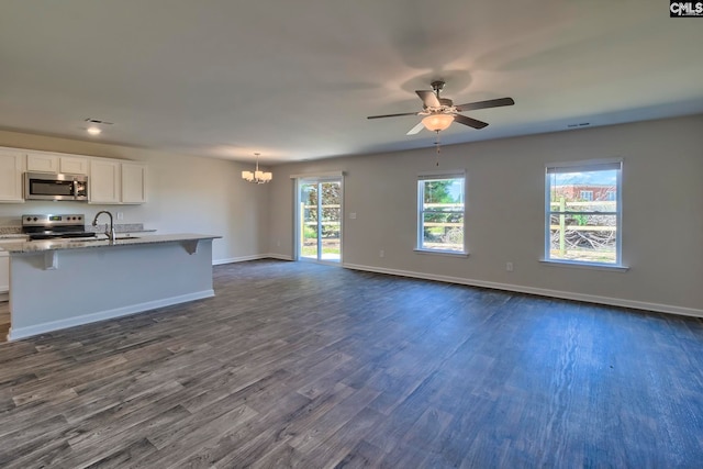 kitchen featuring white cabinets, light stone countertops, appliances with stainless steel finishes, decorative light fixtures, and dark hardwood / wood-style flooring