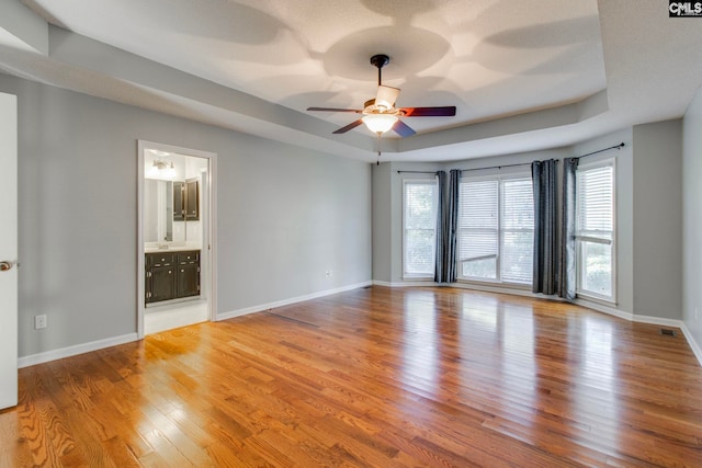 empty room featuring hardwood / wood-style floors, ceiling fan, a healthy amount of sunlight, and a tray ceiling