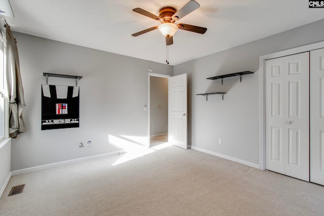 unfurnished bedroom with ceiling fan, a closet, light colored carpet, and a textured ceiling