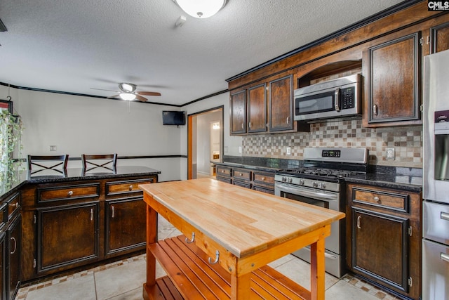 kitchen featuring ceiling fan, decorative backsplash, dark brown cabinets, light tile patterned flooring, and appliances with stainless steel finishes