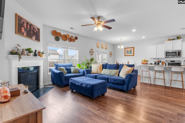 living room with ceiling fan with notable chandelier and dark hardwood / wood-style flooring