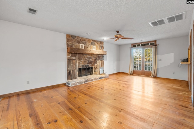 unfurnished living room with a textured ceiling, hardwood / wood-style flooring, a stone fireplace, and ceiling fan