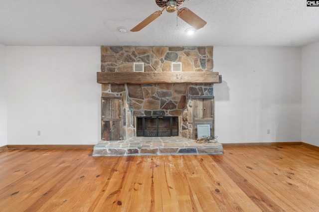 unfurnished living room with a stone fireplace, ceiling fan, a textured ceiling, and hardwood / wood-style flooring