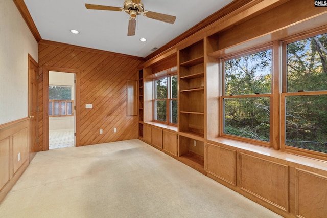 interior space featuring ceiling fan, wood walls, light colored carpet, and crown molding