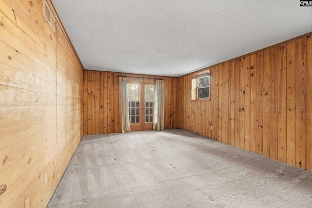 empty room featuring light carpet, french doors, a textured ceiling, and wooden walls