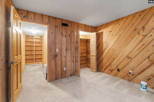 spare room featuring light colored carpet, a textured ceiling, and wooden walls